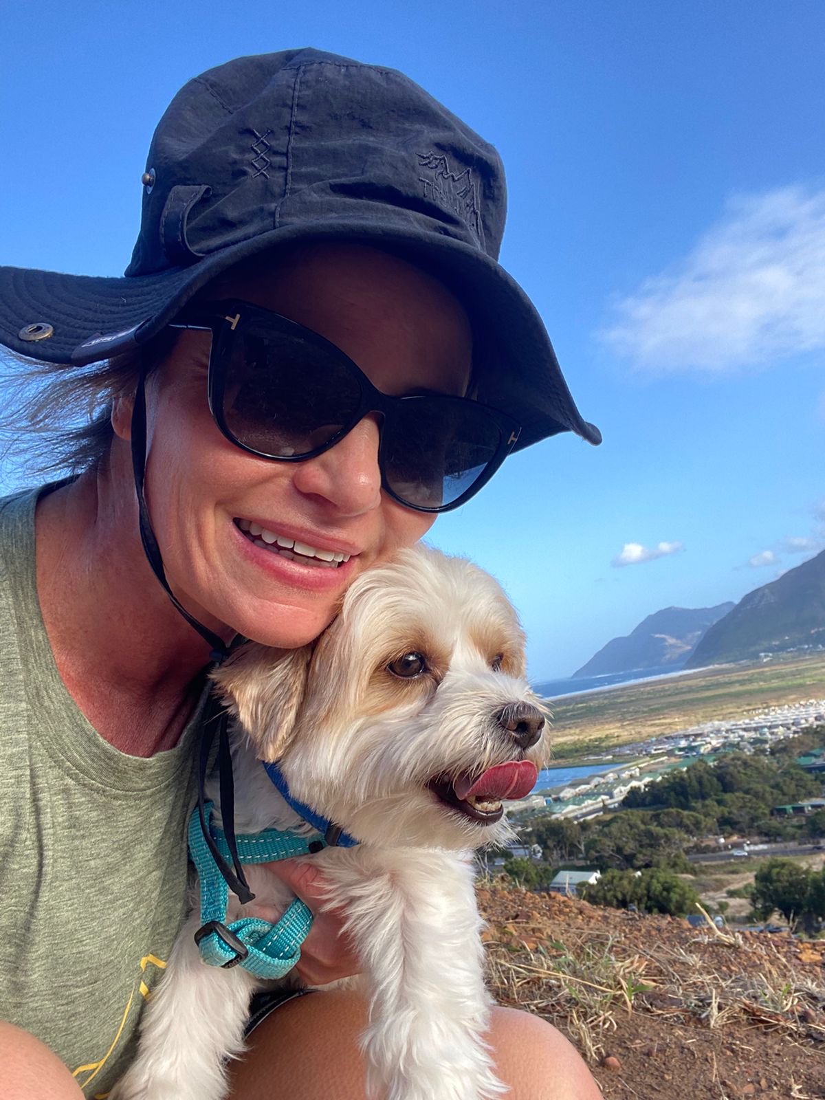 A happy small white dog being cuddled on a sunny hike above Capri with mountain and ocean views